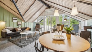 Ein gemütlicher Raum mit hohen Decken, Holzbalken, einem runden Esstisch und einer komfortablen Sitzecke mit Sofa und Sesseln.