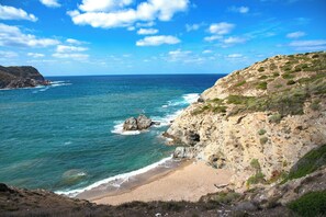 A coastal landscape with a beach, rocky cliffs, and the ocean. - Holiday apartment with air conditioning (Alghero)