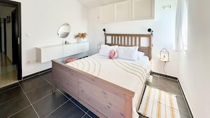 Une chambre à coucher avec un lit en bois, une literie blanche, une table de chevet avec un miroir et un petit objet décoratif accroché au mur.