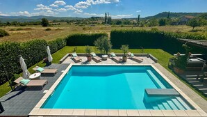 Une piscine rectangulaire dont les bords sont recouverts de carreaux, entourée d’une haie basse et d’une terrasse dallée.