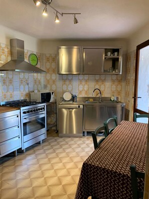 Une cuisine compacte dotée d’appareils électroménagers en acier inoxydable, une table à manger recouverte d’une nappe à motifs et des carreaux de sol à motifs.
