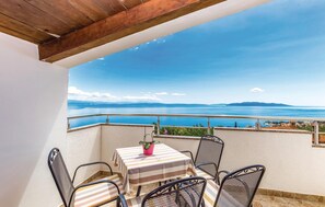 Uma varanda com mesa e cadeiras, com vista para um corpo de água e montanhas ao longe.