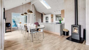 Een moderne keuken met een centraal eiland, een eethoek met een grote tafel en stoelen, en een houtkachel.