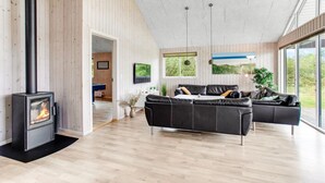 Een ruime woonkamer met een moderne open haard, een zwarte leren bank en een groot raam met uitzicht op de omgeving.