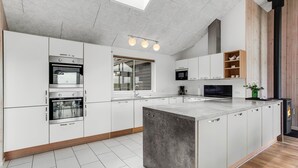 Een moderne keuken met witte kasten, een centraal eiland, inbouwapparatuur en een houten accentmuur.