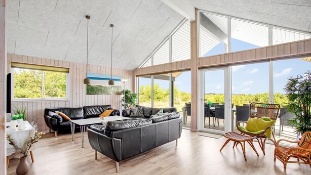 Een ruime woonkamer met een grote leren bank, een eettafel en rieten stoelen.