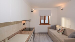 Cocina compacta con horno integrado, una ventana pequeña y un sofá con un cojín.