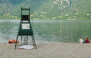 Une tour de surveillance avec un panneau indicateur, une plage de galets et un lac, avec des montagnes en arrière-plan.