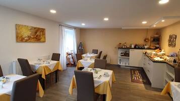 Ein Essbereich mit gedeckten Tischen, eine Küche im Hintergrund und ein Bild an der Wand.