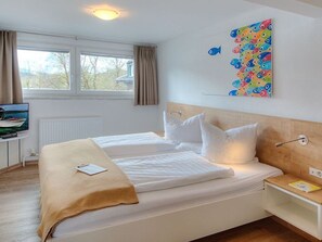 A hotel room with two beds, a TV, a window with curtains, and a colorful fish wall art. - Family room Wildeneck - Seepension Hemetsberger (Mondsee)