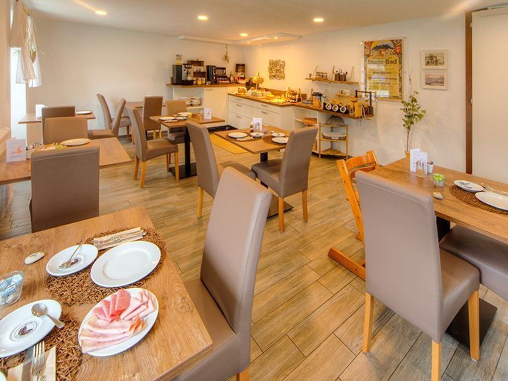 Un espace repas avec des tables et des chaises, une cuisine à l’arrière-plan et une affiche accrochée au mur.