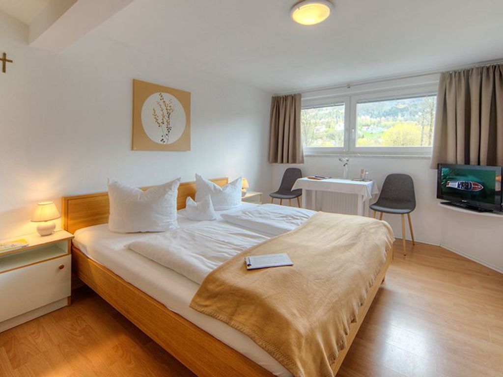 Ein Hotelzimmer mit Bett, Nachttisch, Lampe, Fernseher, Schreibtisch, Stuhl und einem Fenster mit Vorhängen.