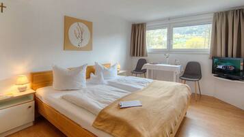 Ein Hotelzimmer mit Bett, Nachttisch, Lampe, Fernseher, Schreibtisch, Stuhl und einem Fenster mit Vorhängen.