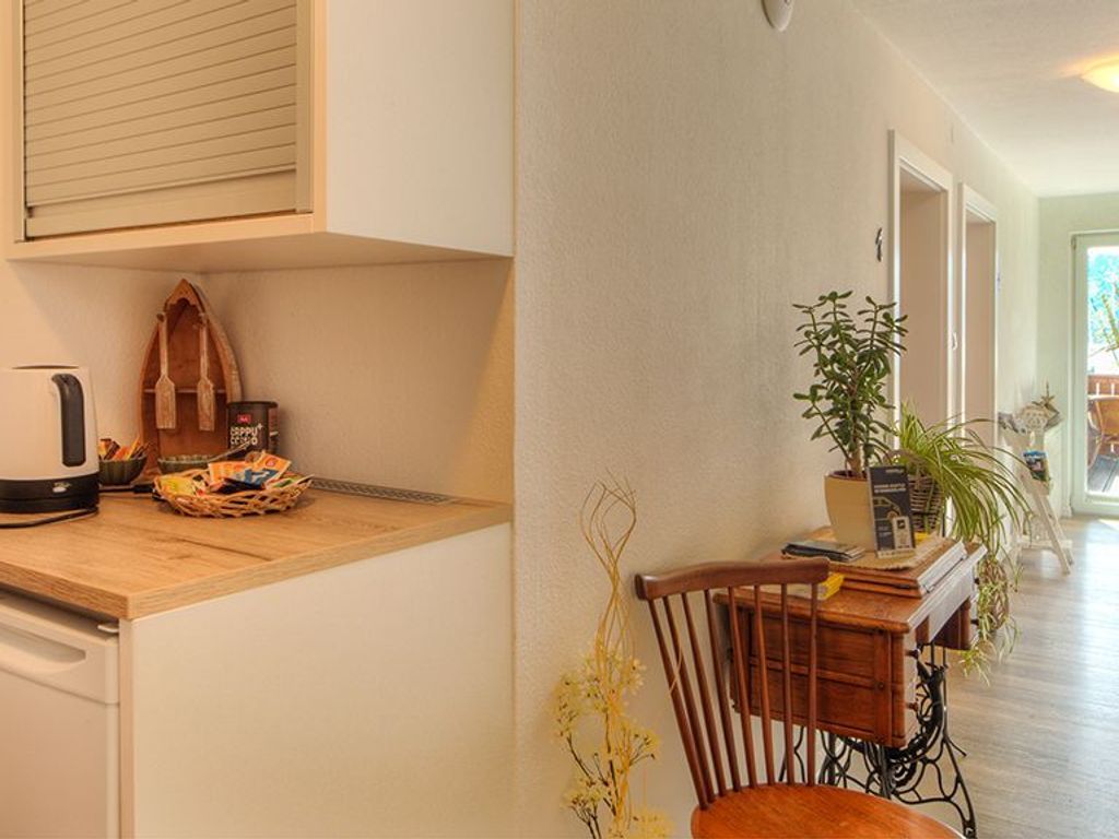 Une cuisine avec un plan de travail en bois, une bouilloire, un panier de collations, une chaise et une plante en pot.
