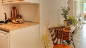 Eine Küche mit Holzausziehtisch, einem Wasserkocher, einer Snack-Korb, einem Stuhl und einer Topfpflanze.