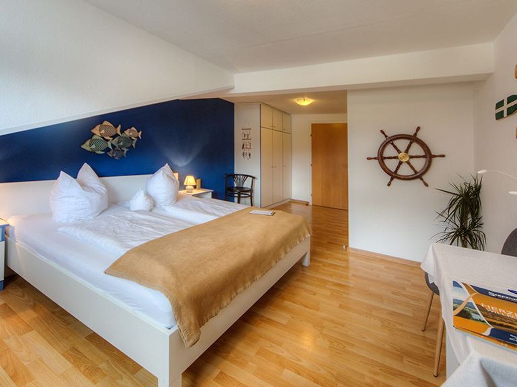 Ein Schlafzimmer mit Bett, Nachttisch, Stuhl, Tisch und einer Wand mit einer Schiffslaugerei.