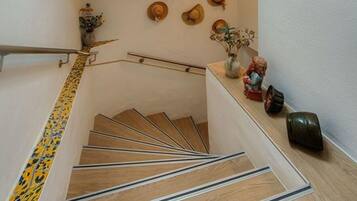 Eine Holztreppe mit Metallgeländer, eine Wand mit dekorativen Hüten und ein kleiner Tisch mit Vase und Figur.