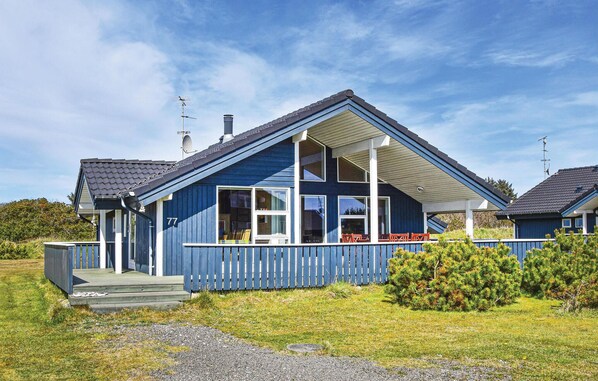 Ein blaues Haus mit Veranda, Hausnummer 77 und einem kleinen Garten.