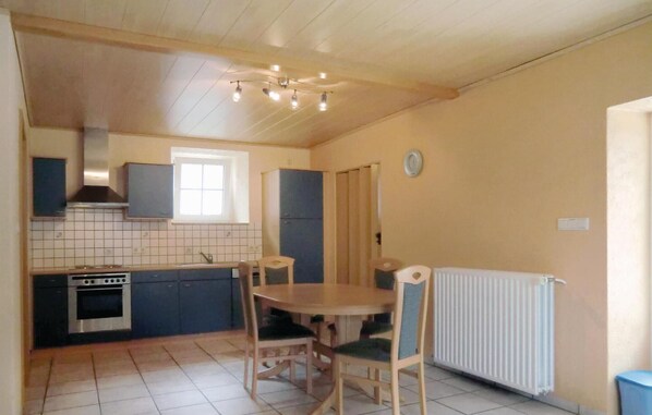 A compact kitchen with a stove, oven, and a window above the sink. There is a dining table with chairs and a radiator on the floor.