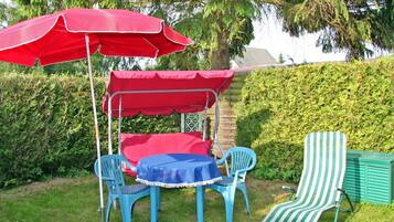 Eine Terrasse mit Tisch und Stühlen, einem roten Sonnensegel und einem gestreiften Stuhl.