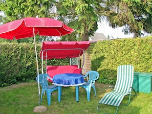 Un patio con una mesa y sillas, un dosel rojo y una silla a rayas.