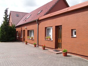 A red brick building with a tiled roof, multiple windows, and potted plants on the ground floor. - Vacation Rental I - Anika's Vacation Rentals (Zarrendorf)
