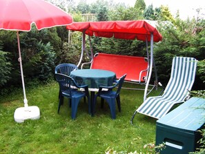 A patio with a table and chairs, a swing set, and a striped lounge chair. - Vacation Rental I - Anika's Vacation Rentals (Zarrendorf)