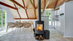A modern kitchen with a wood-burning stove, white cabinets, and a dining area with wicker chairs. - Lovely home in Ulfborg with WiFi (Ulfborg)