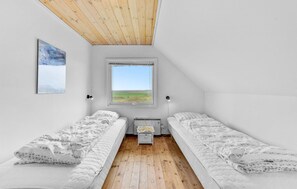 Un petit logement composé d’une seule pièce, comprenant deux lits simples, un plafond en bois, une grande fenêtre donnant sur la campagne et un tableau accroché au mur.