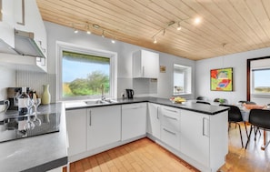 Une cuisine moderne avec des meubles blancs, une grande fenêtre et un coin repas comprenant une table et des chaises.