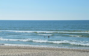 Une plage avec des vagues et deux personnes dans l’eau.
