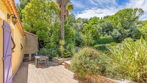 A patio with a table and chairs, surrounded by lush greenery and a stone wall. - Pet friendly home in Roujan (Roujan)