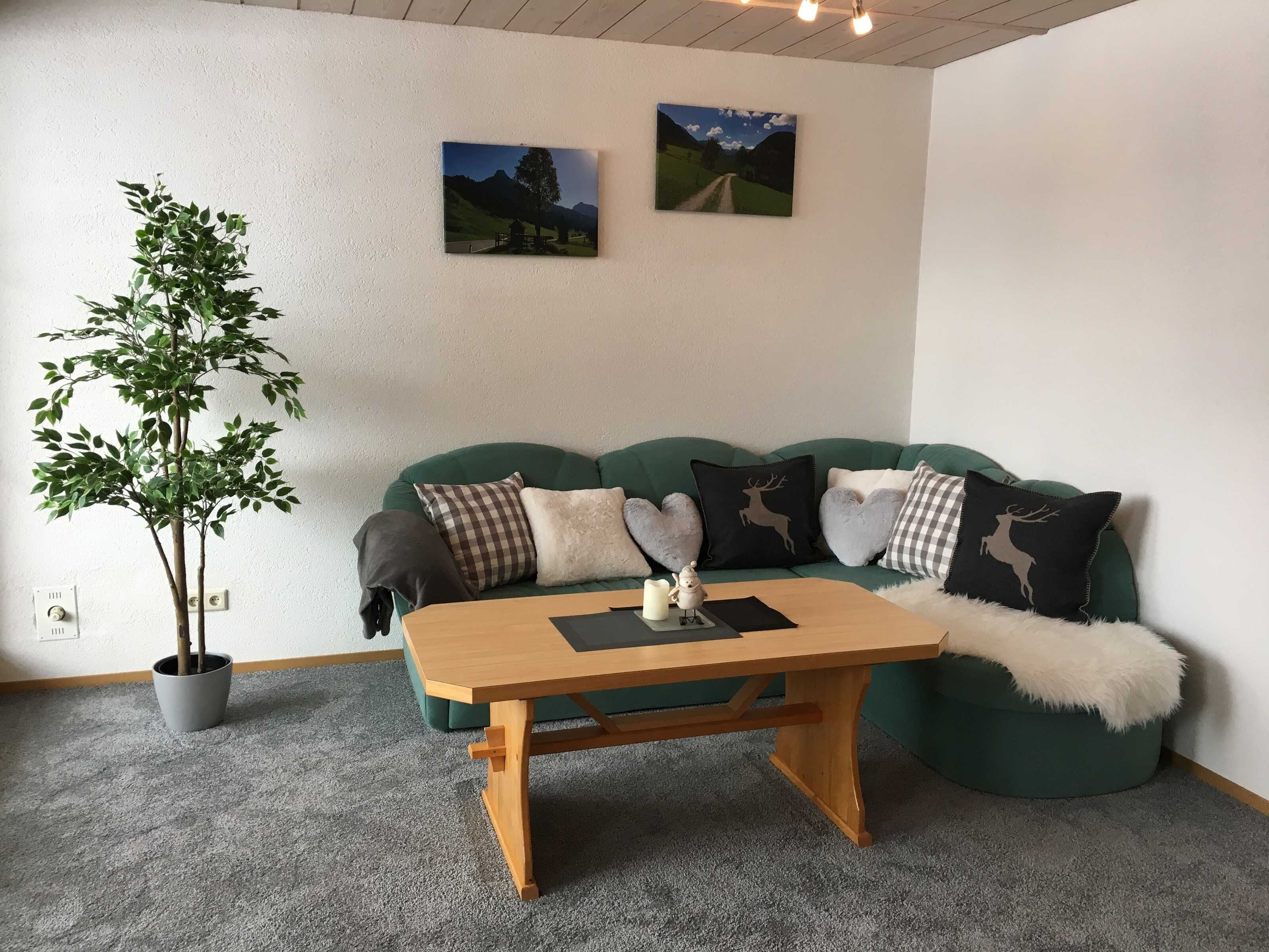 A cozy living room with a green sofa, a wooden coffee table, a potted plant, and two wall-mounted pictures.