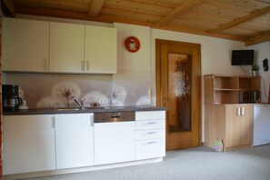 Una cocina con armarios blancos, una puerta de madera, un reloj y un televisor en la pared.