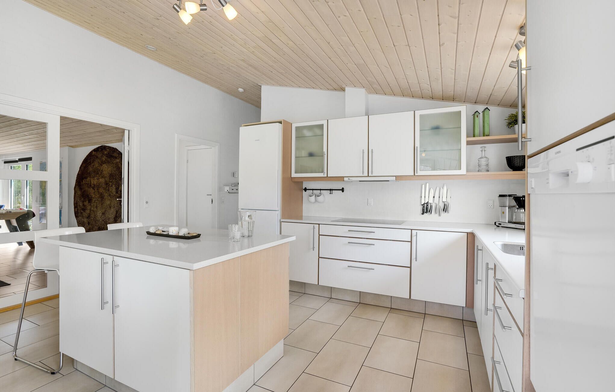 Une cuisine moderne avec des meubles blancs, un îlot central et un plafond en bois.