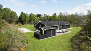 A modern black house with a sloped roof, a patio with outdoor furniture, and a swing set in a grassy yard surrounded by trees. - Beautiful home in ålbæk with WiFi (Ålbæk)