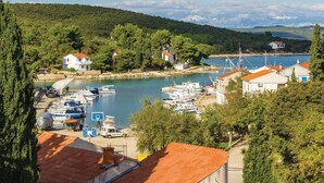 Un village côtier où des bateaux sont amarrés dans une marina, entouré d’une végétation luxuriante et avec des collines en arrière-plan.