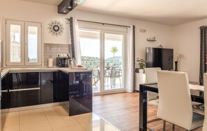 Eine moderne Küche mit einer großen Kücheninsel, ein Essbereich mit Tisch und Stühlen sowie eine Glastür, die auf einen Balkon mit Blick auf die Hügel führt.