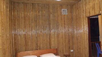 Een kamer met een bed, een houten hoofdbord, een ventilator aan de muur en een kleine tafel.