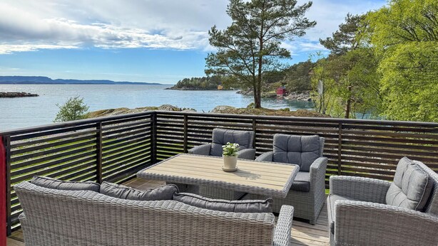 Une terrasse dotée de meubles en osier, d’une table et offrant une vue sur un lac et des montagnes lointaines.