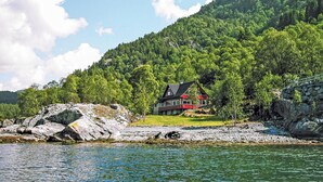Une maison au bord d’un lac, avec une colline boisée en arrière-plan.