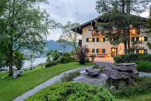 A multi-story building with a balcony, surrounded by greenery and a view of a lake.