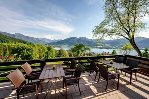 Une terrasse extérieure avec des tables et des chaises, offrant une vue sur un lac et des montagnes.