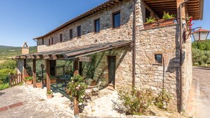 Een stenen huis met een overdekte patio, zitplaatsen buiten en uitzicht op het platteland.