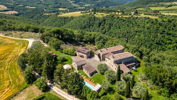 Luchtbeeld van een landgoed met meerdere stenen gebouwen, een zwembad en omliggende velden.