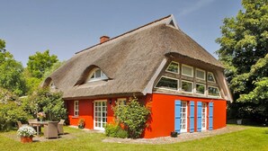 Ein Haus mit einem Strohdach, roten Wänden und blauen Fensterläden.