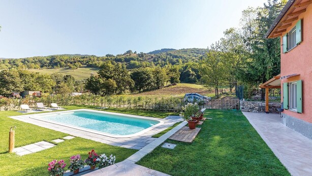 Une piscine offrant une vue dégagée sur le paysage environnant, une pelouse bien entretenue et un bâtiment doté d’une façade en pierre.