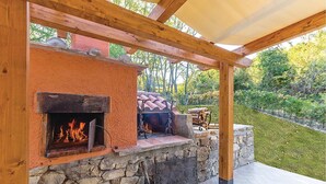 Une cheminée extérieure en pierre, dotée d’une hotte, d’un barbecue et d’un mur en pierre.