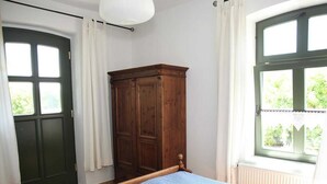 A room with a bed, a wooden wardrobe, a window with a view of greenery, and a door. - Apartment IV - Apartments in farmhouse - Property 44365 (Papendorf)