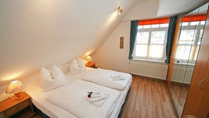 Un dormitorio con cama, mesitas de noche, una ventana con cortinas y un radiador.